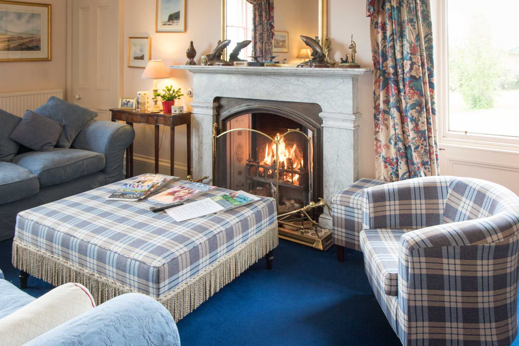 Drawing room with an open log fire, marble mantelpiece and check armchairs