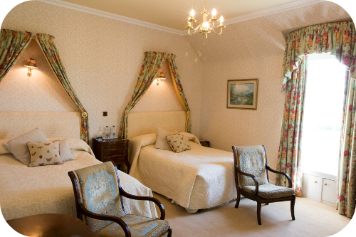 Twin bedroom with canopied drapes above each bed and floral curtains
