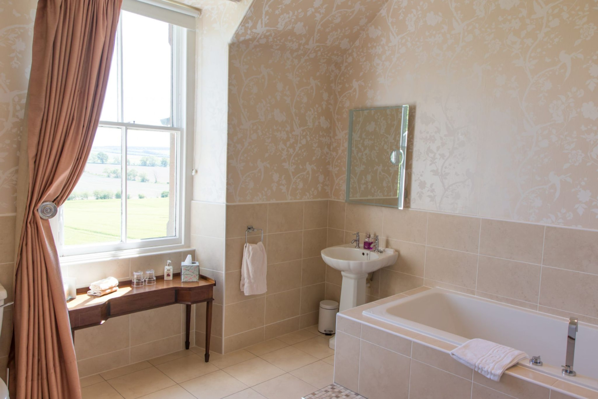 Bathroom with bath, pedestal basin and a sash window overlooking open fields