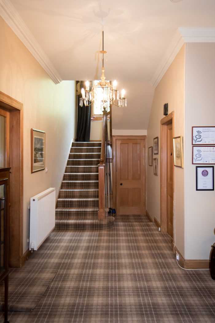 Entrance hall with tartan carpet, chandelier and wooden staircase